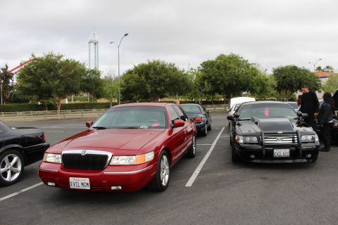 2003 Ford Crown Victoria - dark-red Mercury Grand Marquis sedan with vanity plate EVIL MGM parked beside a black sedan at an outdoor car meet under overcast skies.