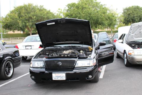2003 Ford Crown Victoria - black Mercury full-size sedan with its hood raised exposing the engine, wearing California plate 4ZDY503, parked among other cars.