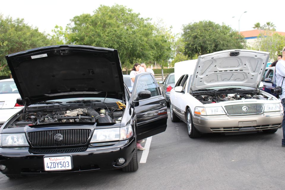 Black sedan and gold Mercury sedan with hoods up, people nearby