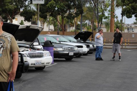 2003 Ford Crown Victoria - line of black, white and gray full-size sedans with hoods open while two men converse in an asphalt parking lot at a car meet.