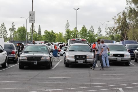 2003 Ford Crown Victoria - Three Ford full-size sedans parked nose-out in a lot as two men in caps walk between them at an outdoor car gathering.
