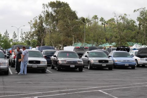 2003 Ford Crown Victoria - long diagonal row of black, gray, blue and white full-size sedans parked at an outdoor car meet as two men inspect the nearest cars.