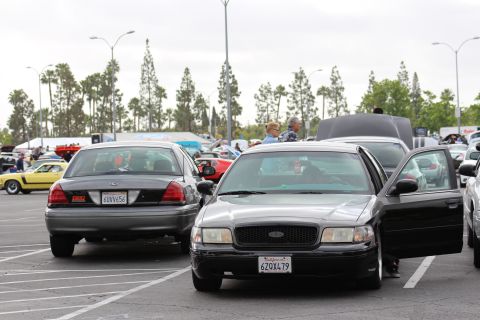 2003 Ford Crown Victoria - gray-black Ford full-size sedan with its driver door open and plate 6ZQX479, with a black sedan beside it at a crowded car meet.
