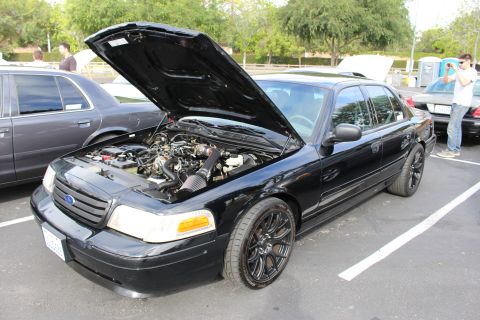 2003 Ford Crown Victoria - black Ford Crown Victoria sits with its hood raised on black alloy wheels while a man photographs it.