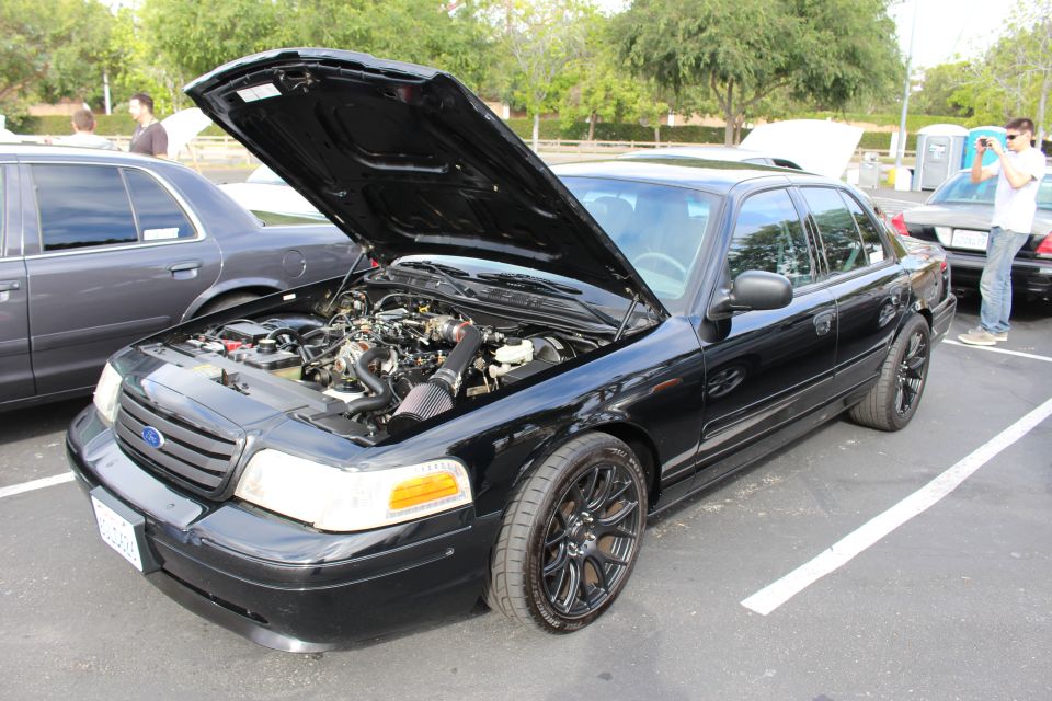 Black Ford Crown Victoria with hood open and black wheels in a lot