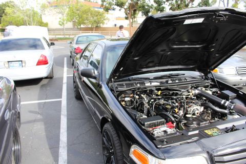 2003 Ford Crown Victoria - black Ford sedan displays its engine bay with a red intake tube, parked next to a white sedan at a meet.