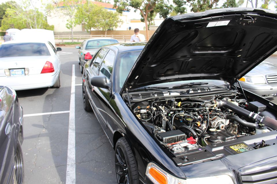 Black Ford sedan engine bay with red intake tube beside white sedan