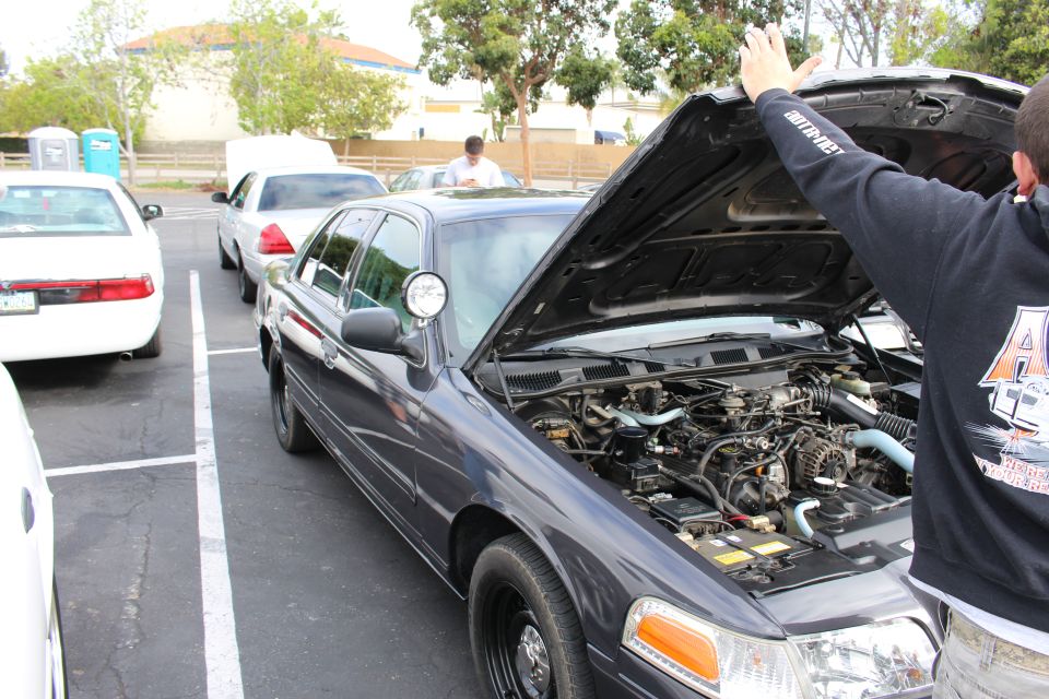 Dark gray Ford Crown Victoria with hood being raised in a lot