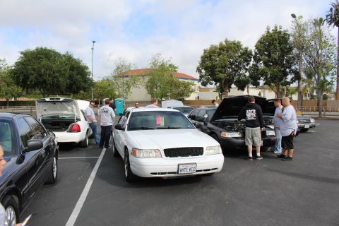 2003 Ford Crown Victoria - white Ford Crown Victoria sits front and center in a lot full of Panther sedans with people milling around.