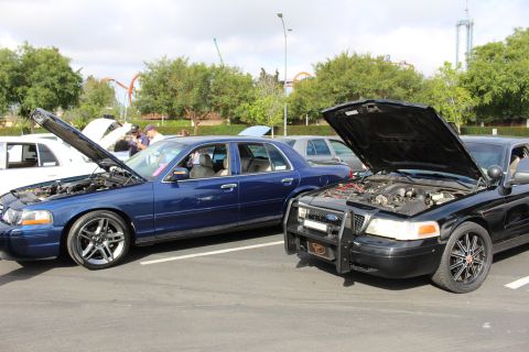 2003 Ford Crown Victoria - blue Ford Crown Victoria parks beside a black sedan with a brush guard, both hoods open, near a theme park.