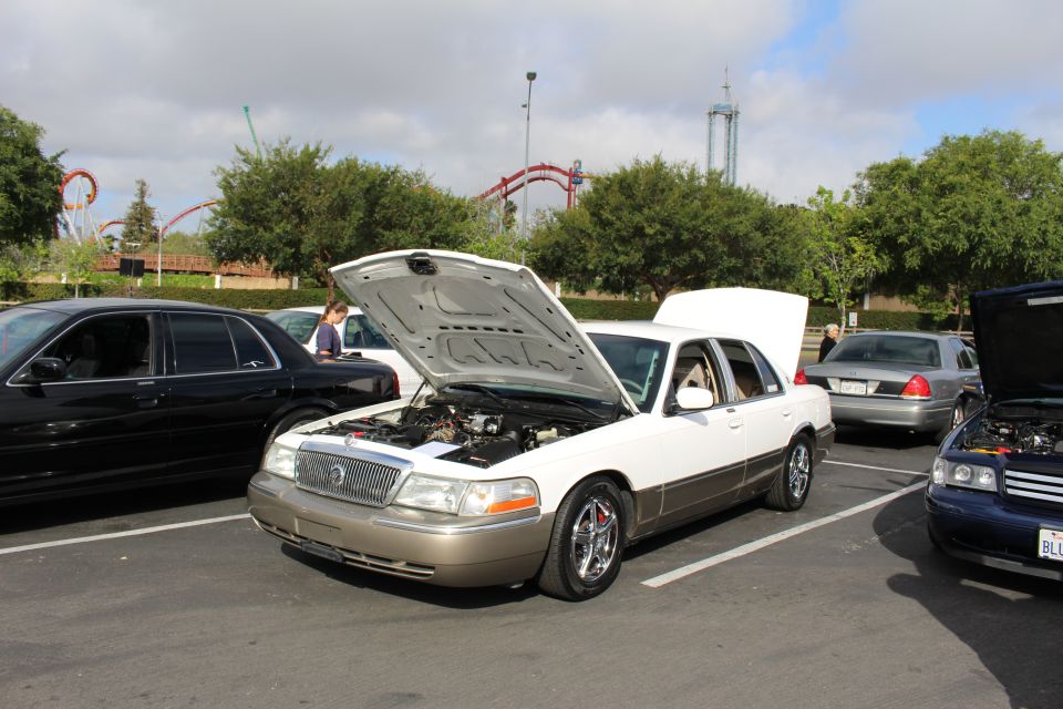 White-over-gold Mercury sedan with hood open at a car show near a coaster