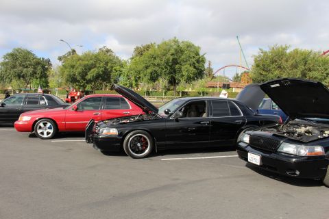 2003 Ford Crown Victoria - lowered black sedan on dark wheels sits between a red sedan and another car at an outdoor car meet.