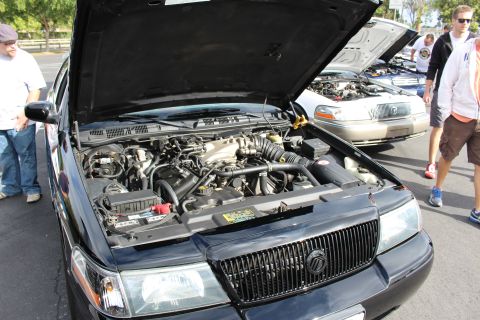 2003 Ford Crown Victoria - Close view of a Mercury sedan's V8 engine bay under a raised hood, with people standing nearby at a car show.