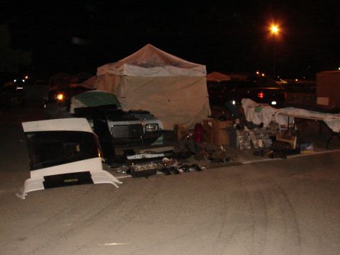 1973 Ford Ranchero - A collection of car parts and debris are displayed on the ground at night, with tents and a car visible in the distance.