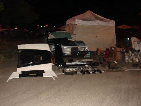 1973 Ford Ranchero - Disassembled vehicle parts, including a white cab and front end, are spread across pavement under a tent at night.