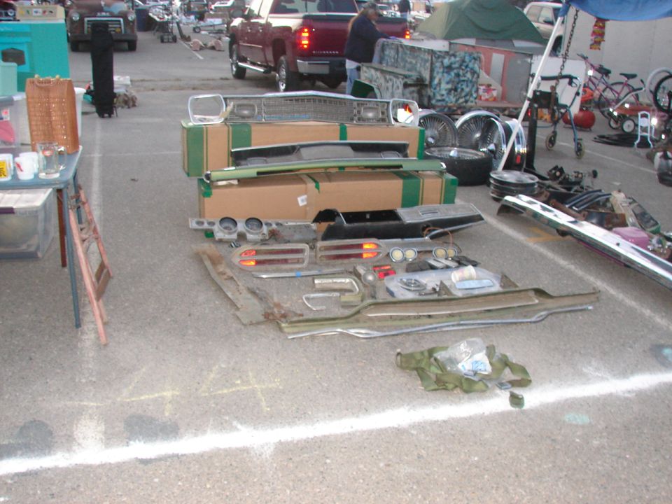 Car parts laid out on pavement, including a grille, taillights, and dashboard components
