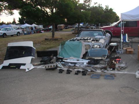 1973 Ford Ranchero - Various car parts are displayed on the ground at an outdoor event, with a partially covered vehicle nearby.