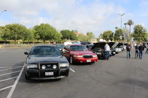 2003 Ford Crown Victoria - black Ford sedan with a push bar leads a row that includes a red sedan at an outdoor parking-lot car show.