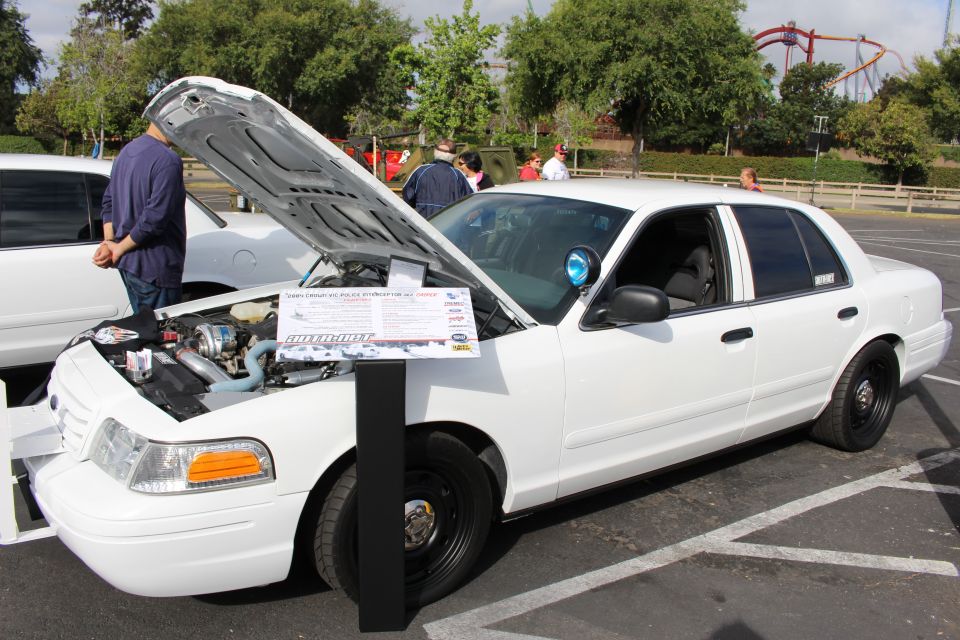 White Ford Crown Victoria with open hood and spec card at a car show