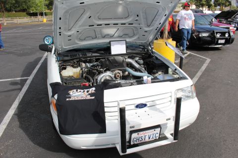 2003 Ford Crown Victoria - white Ford sedan displays a supercharged engine under a raised hood with an ADTR banner and 'GHST VIC' plate.