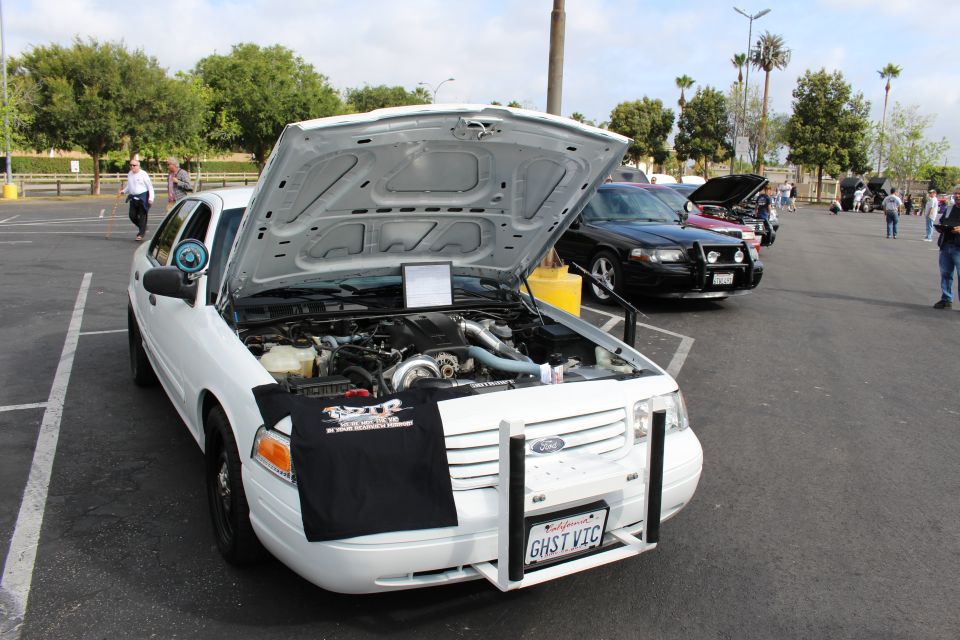 White Ford Crown Victoria sedan with hood open at an outdoor car show