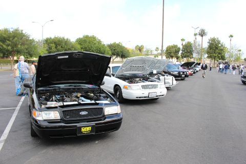 2003 Ford Crown Victoria - black Ford Crown Victoria with open hood leads a long row of sedans at an outdoor car show with onlookers nearby.