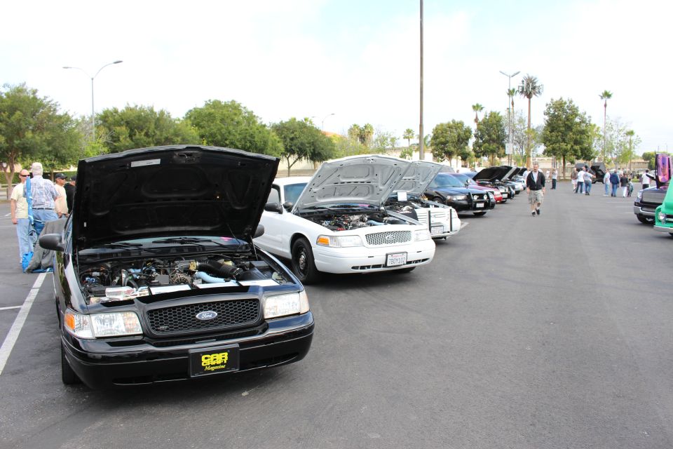 Black Ford Crown Victoria with open hood at front of a car-show row