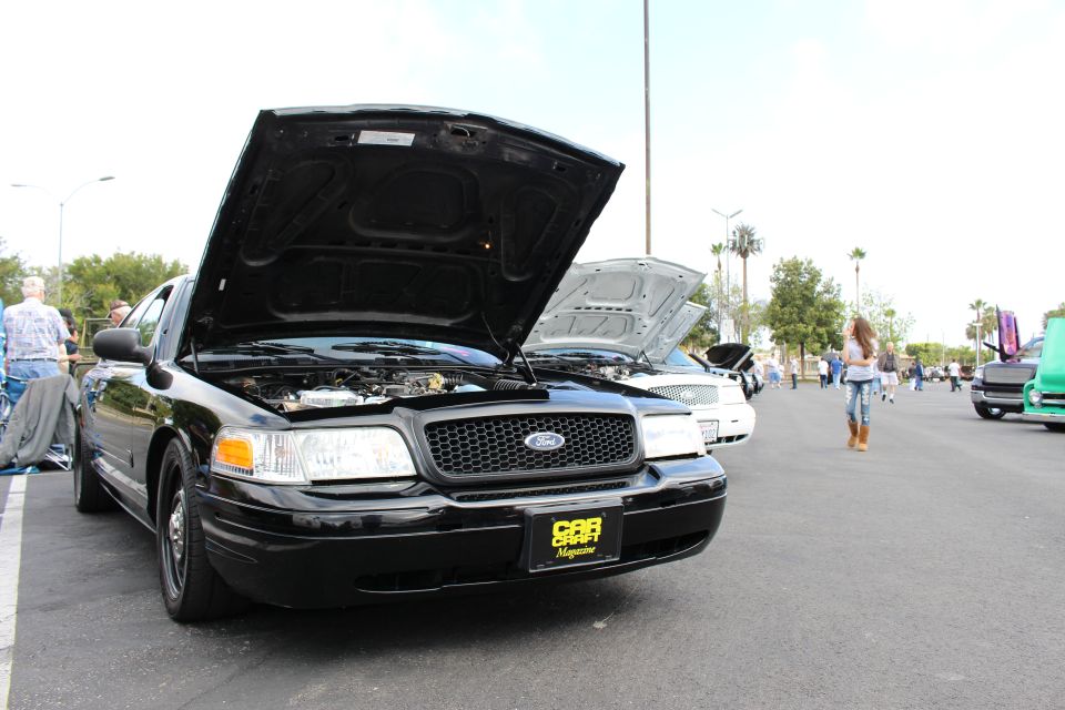 Black Ford Crown Victoria with open hood and magazine placard at a show
