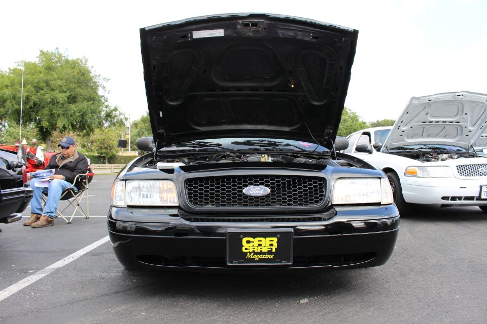 Head-on view of a black Ford Crown Victoria with open hood at a show