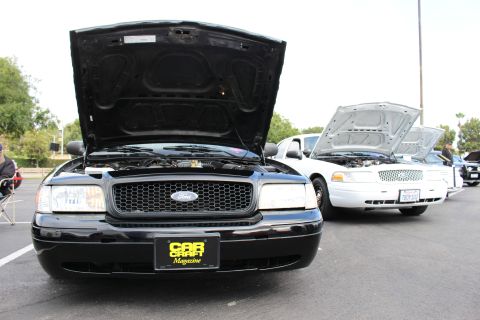 2003 Ford Crown Victoria - Front of a black Ford Crown Victoria with a Car Craft Magazine sign, parked next to a white Ford sedan with open hood.