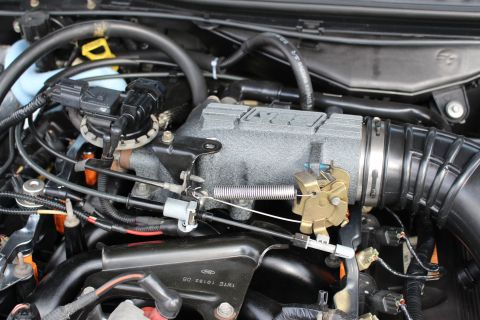 2003 Ford Crown Victoria - Close-up of an engine intake manifold, throttle body linkage, and air intake duct within a vehicle engine bay.