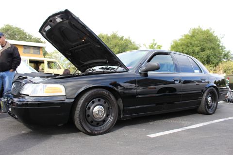 2003 Ford Crown Victoria - glossy black Ford Crown Victoria with open hood and black steel wheels displayed at an outdoor car show.