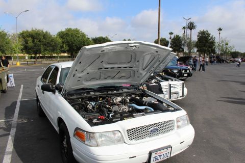2003 Ford Crown Victoria - white Ford Crown Victoria with raised hood parked at an outdoor car show with attendees and other cars in the lot.