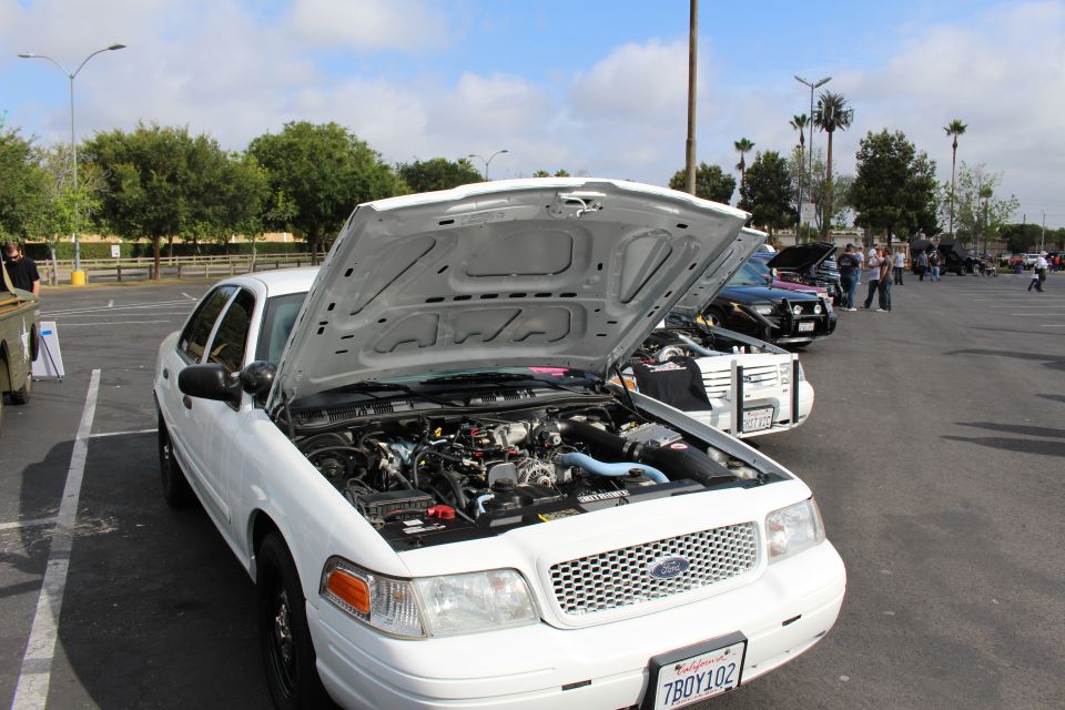 White Ford Crown Victoria with open hood at an outdoor car show