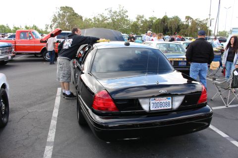 2003 Ford Crown Victoria - Rear view of a black Ford Crown Victoria sedan with open trunk surrounded by people at a busy outdoor car show.