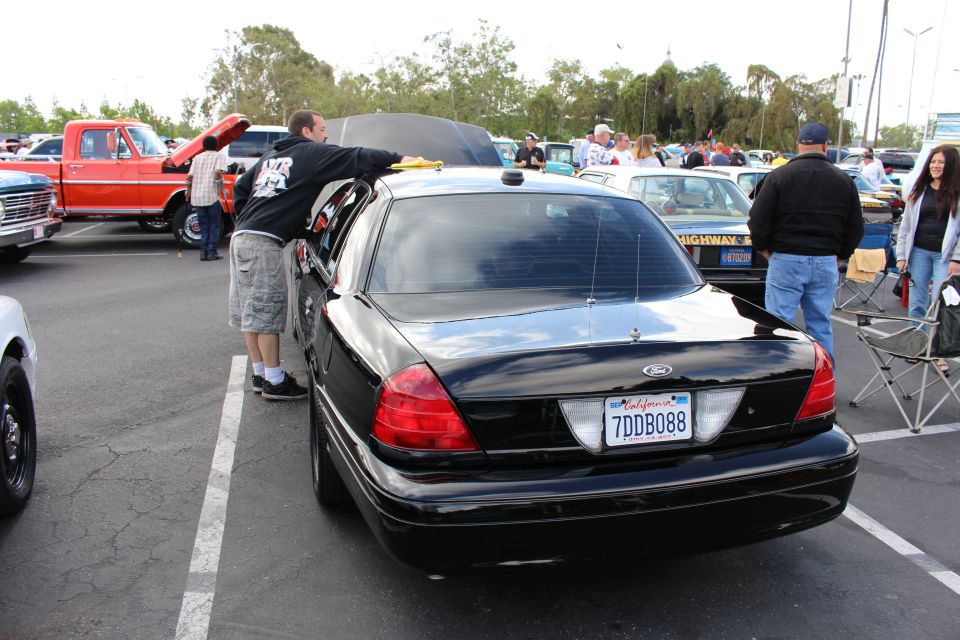 Rear of a black Ford Crown Victoria sedan at a busy car show