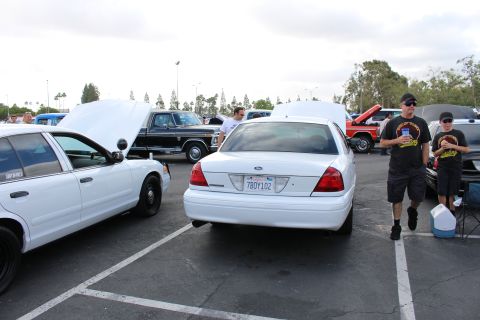 2003 Ford Crown Victoria - Rear view of a white Ford Crown Victoria parked among other vehicles at an outdoor car show with attendees walking by.