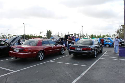 2003 Ford Crown Victoria - maroon sedan and a black sedan park side by side in a striped lot as people gather near open trunks behind them.