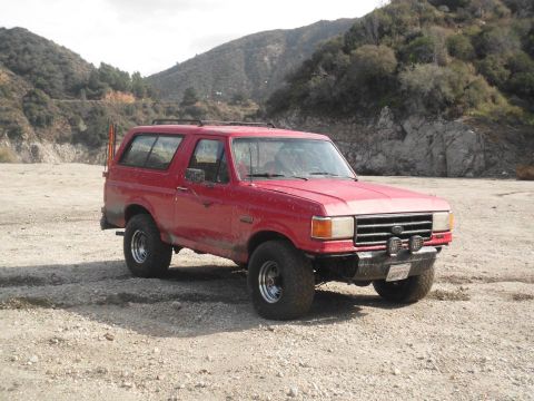 1988 Ford Bronco - Red 1988 Ford Bronco sits in a dry, rocky area with hills behind it.