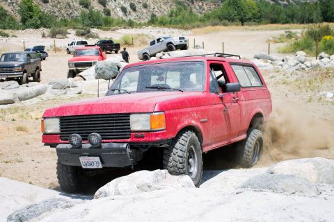 1988 Ford Bronco - This red SUV is navigating a rocky trail, with several other vehicles visible in the background.