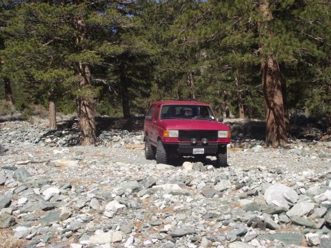 1988 Ford Bronco - A red SUV is parked in a rocky, wooded area.