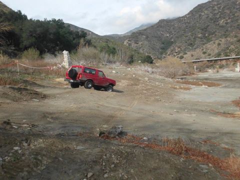 1988 Ford Bronco - A red 1988 Ford Bronco navigates a dusty, off-road trail with mountains in the background.