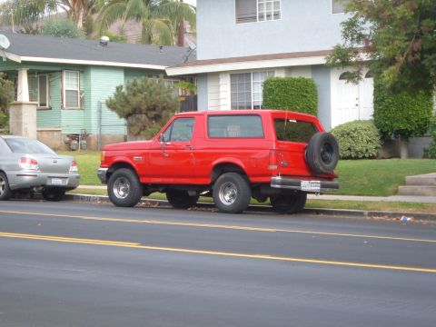 1988 Ford Bronco - This red 1988 Ford Bronco is parked on a residential street, showing its side profile and spare tire on the back.