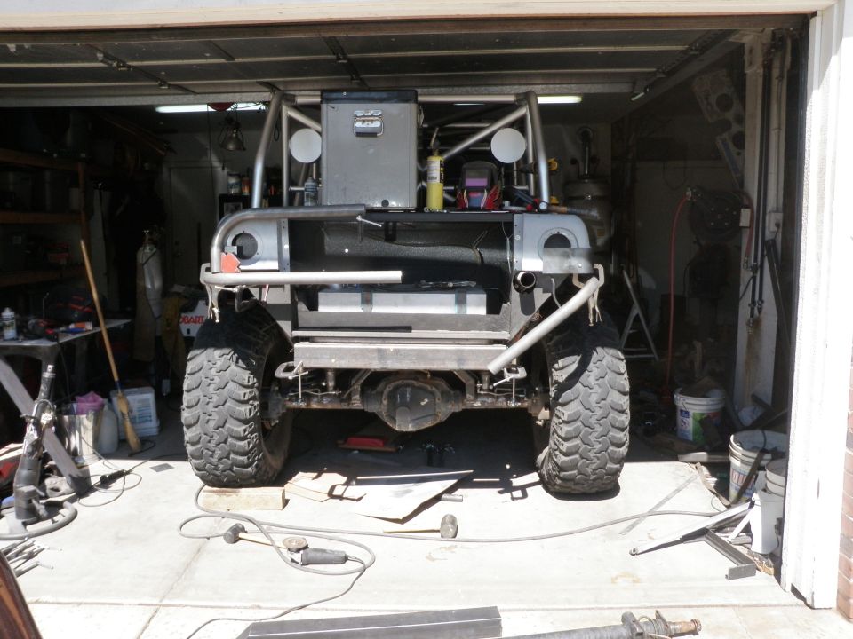 Off-road vehicle rear view, modified with roll cage, large tires, and custom bumper, in a garage