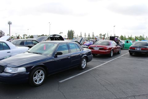 2003 Ford Crown Victoria - dark blue Ford sedan on alloy wheels sits at the front of a parking-lot car show with maroon and green cars lined up behind it.