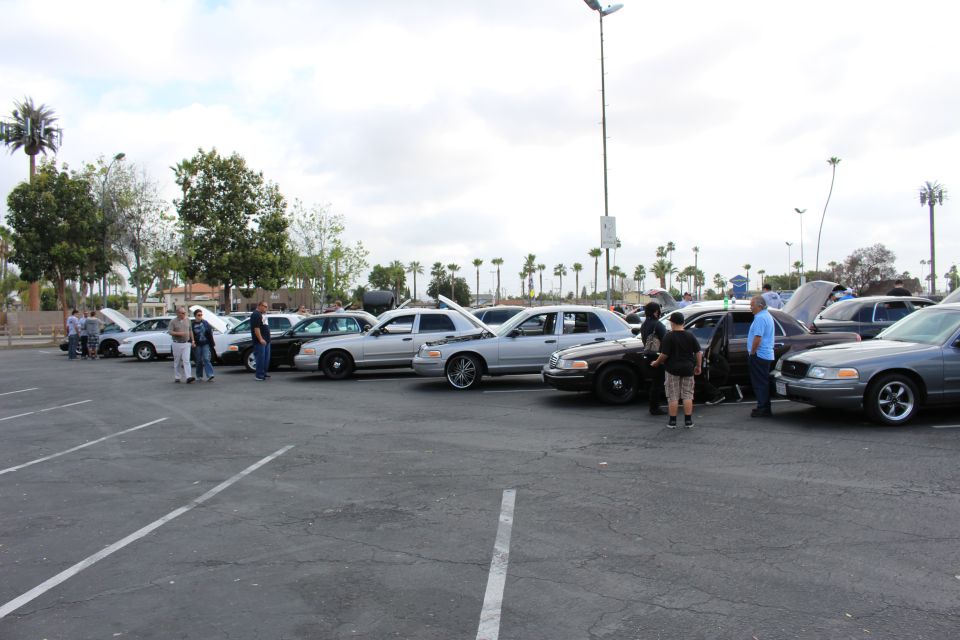 Silver and dark sedans angled in a lot with attendees gathered around