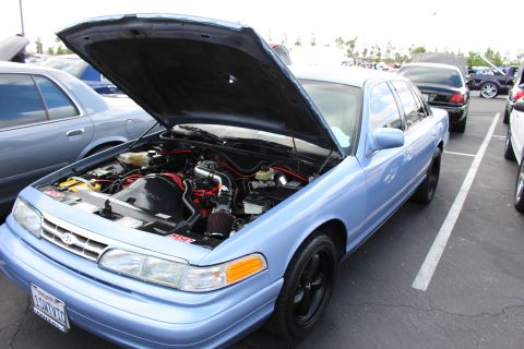 2003 Ford Crown Victoria - light-blue Ford full-size sedan sits with its hood raised, revealing a detailed engine bay with red wiring, on black steel wheels.