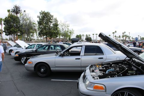2003 Ford Crown Victoria - silver Ford sedan with raised hood is lined up beside a black sedan in a busy parking-lot car meet under cloudy skies.