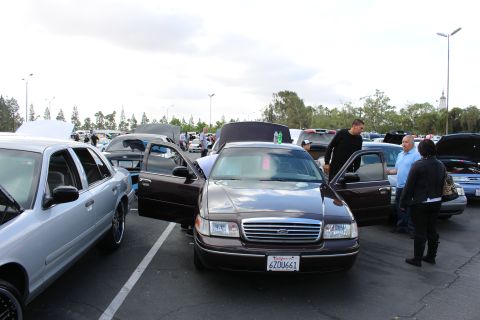 2003 Ford Crown Victoria - dark brown Ford sedan with both front doors open displays California plate 6ZOU661 as spectators stand nearby at a car meet.