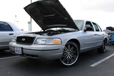 2003 Ford Crown Victoria - Front three-quarter view of a silver Ford sedan with its hood raised, fitted with large black-and-chrome multi-spoke wheels.